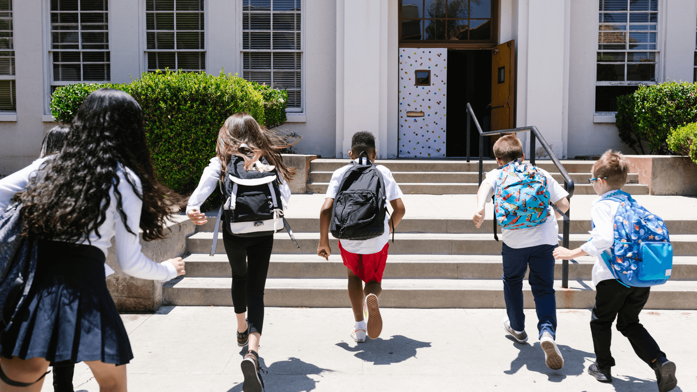 Children with backpacks running towards a school building, representing students ready for a back-to-school eye exam for clear vision.