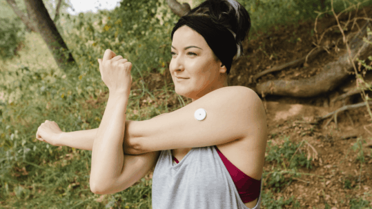 Woman with a continuous glucose monitor (CGM) stretching outdoors, representing active lifestyle and diabetes management for eye health.