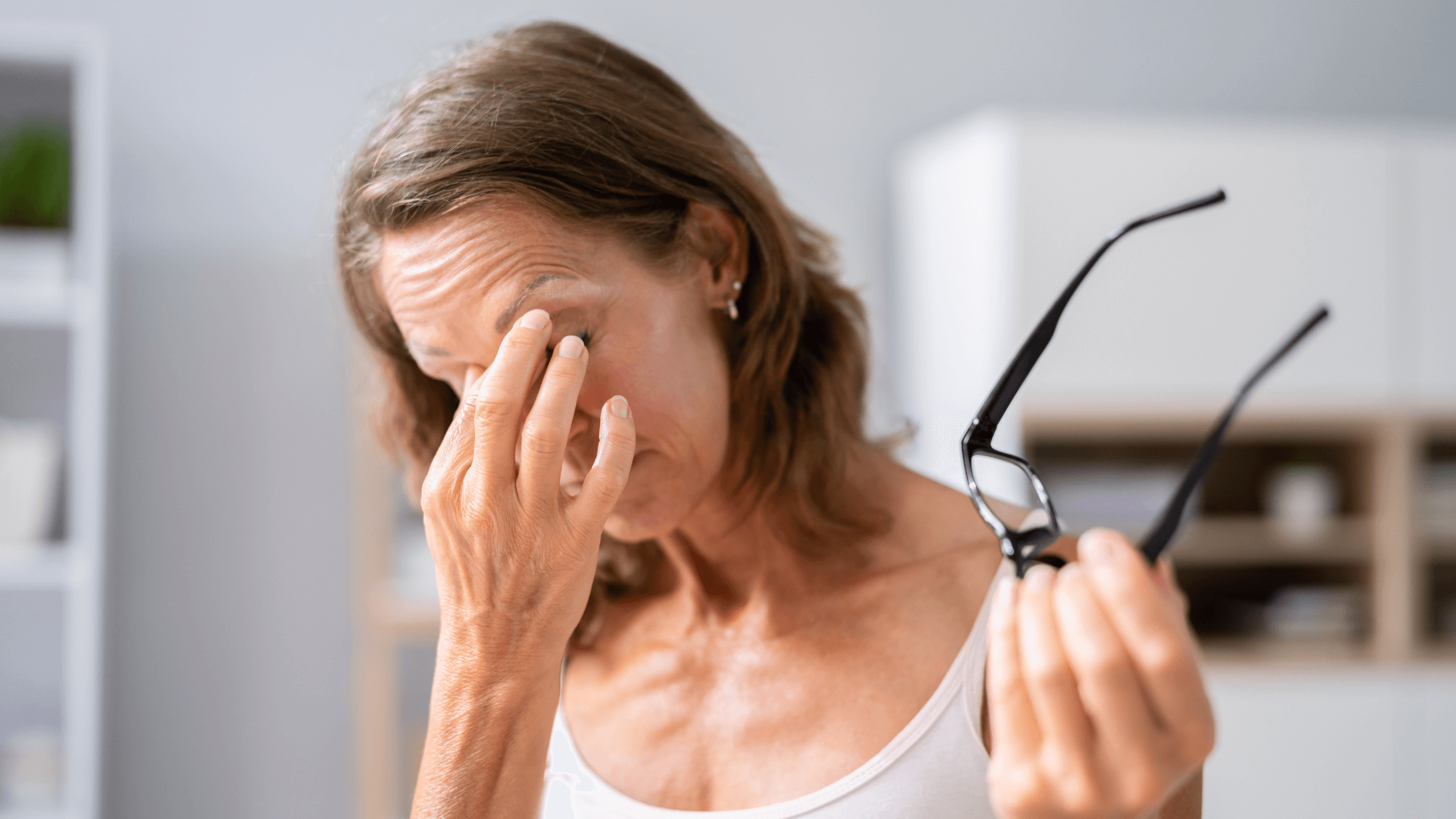 Woman rubbing her eye and holding glasses, indicating eye strain or discomfort possibly related to glaucoma symptoms or a need for an eye exam