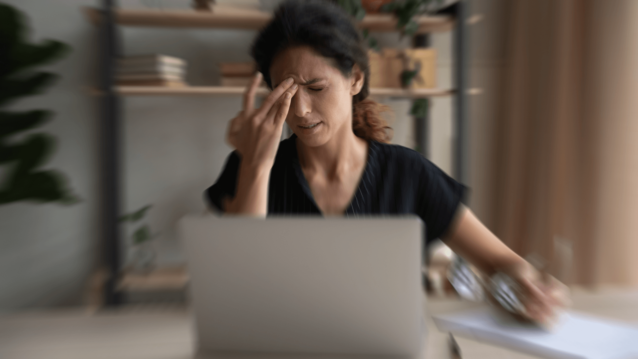Woman rubbing her eyes while using a laptop, showing blurred vision and eye strain, common cataract warning signs.