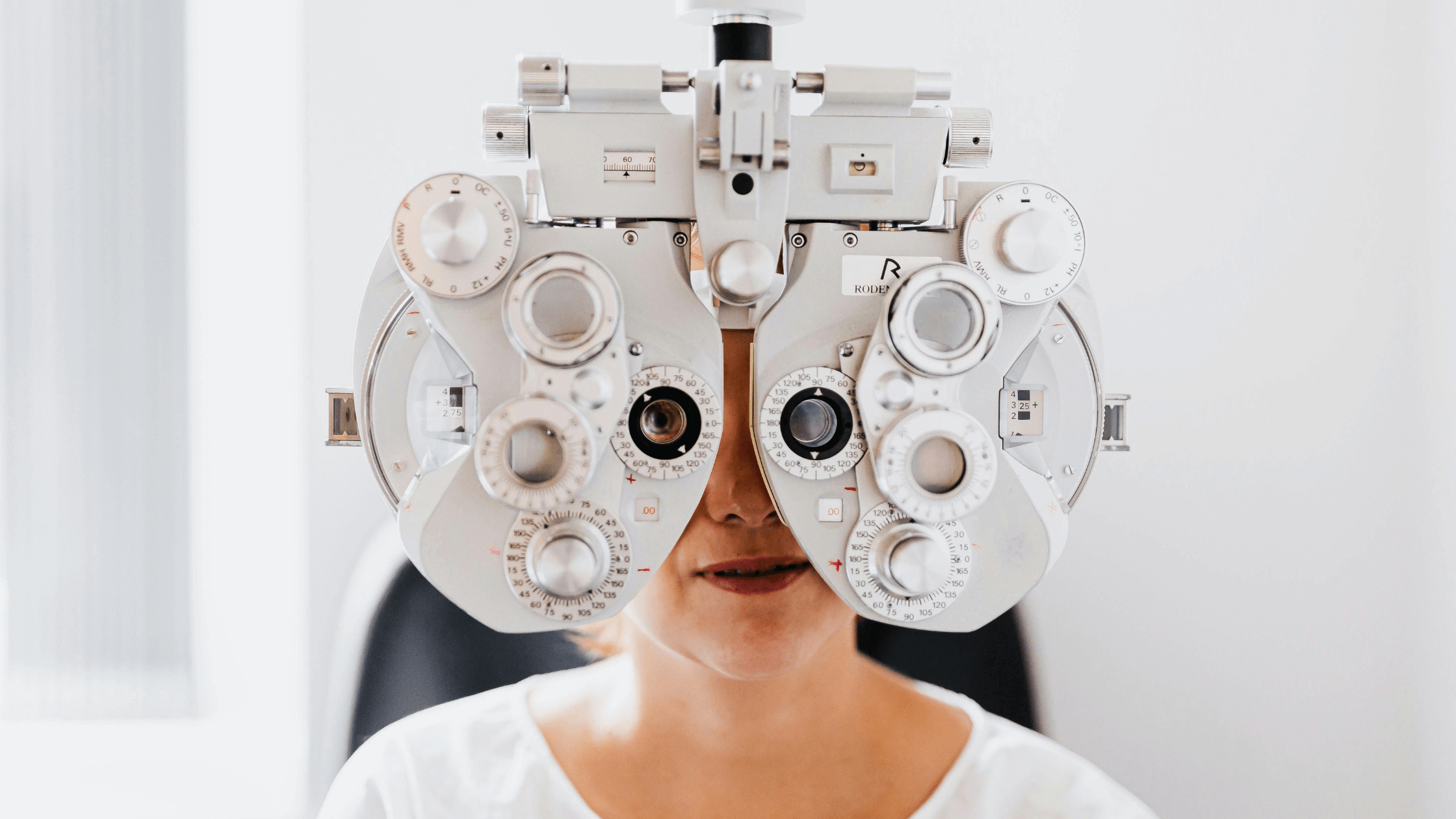 A patient looking into a phoropter during a comprehensive eye exam to determine their vision prescription.