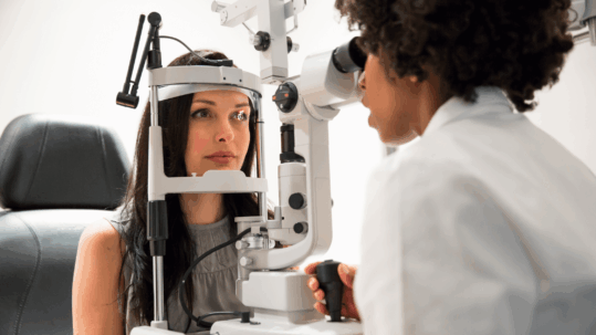 An ophthalmologist examining a patient's eyes with a slit lamp machine during a comprehensive eye exam to check for macular degeneration.