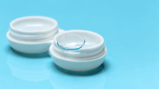 A close-up image of a specialty contact lens resting on a finger, highlighting the lens's design for use in Scleral lenses and dry eye treatment.