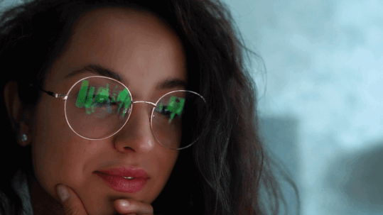 A woman wearing glasses with blue light filtering lenses, showing a soft reflection of a computer screen, symbolizing relief from digital eye strain.