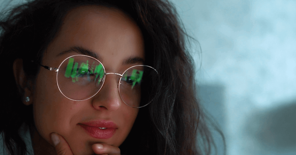 A woman wearing glasses with blue light filtering lenses, showing a soft reflection of a computer screen, symbolizing relief from digital eye strain.