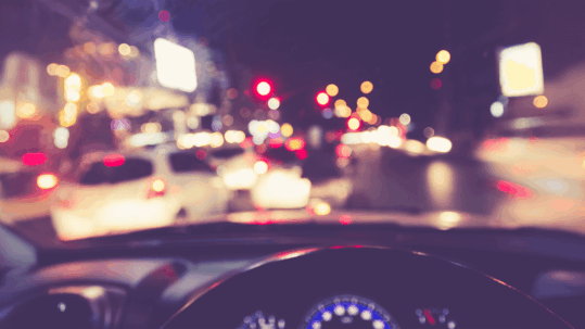 A driver's perspective at night showing blurry, haloed headlights and streetlights, illustrating the hazards caused by night vision problems like cataracts and astigmatism.