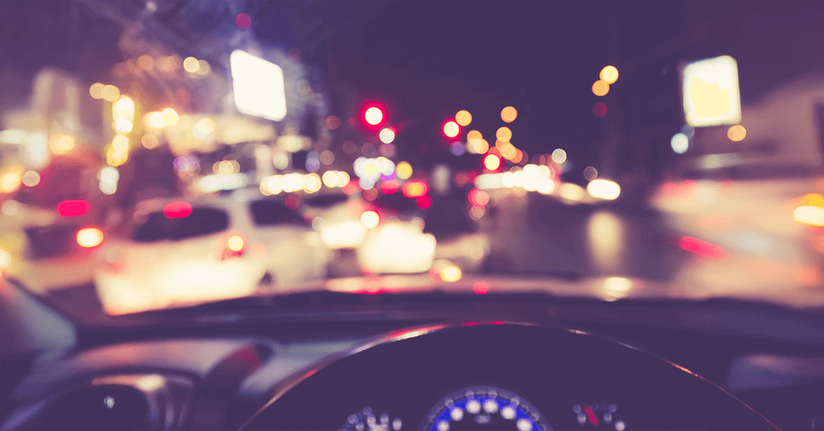 A driver's perspective at night showing blurry, haloed headlights and streetlights, illustrating the hazards caused by night vision problems like cataracts and astigmatism.